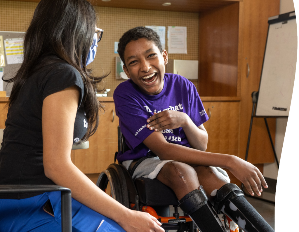 A teen sitting on a wheelchair with smile, talking with a hospital staff