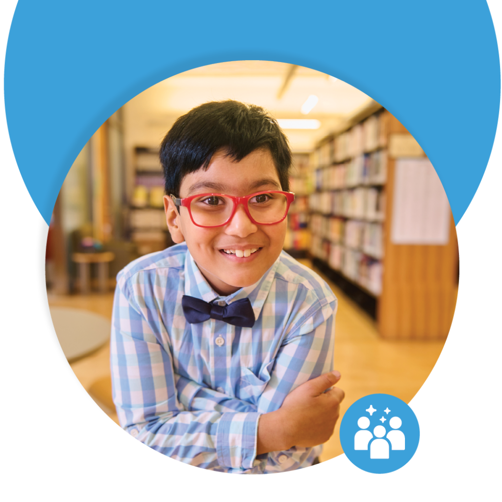 A boy wearing glasses smiling in front of some bookshelf full of books.